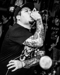 man with tattooed arms singing in a microphone