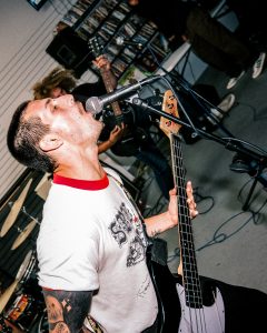 image of a man from the band Flak singing into a microphone while holding an electric guitar