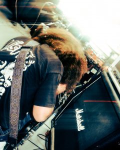 photo of a musician from the band Flak standing next to an amp and holding a guitar