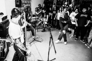 black and white photo of a performance from the band Flak, musicians are performing on the left, a few people are dancing with the audience standing behind them