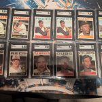 12 graded baseball and basketball trading cards in acrylic display cases. The cards read: "Yankees: Mickey Mantle, outfield, 5.5," "Yankes: Mickey Mantle, outfield, 6," "Pirates, Bob Clemente, outfield, 3," "Pirates, Bob Clemente, outfield, 7," "Giants, Willie McCovey, 7.5," "Braves, Hank Aaron, outfield, 3.5," "Cubs, Lou Brock, outfield, 6," "Reds, Pete Rose, 2nd Base, 4.5," "Yankees, Yogi Berra, manager, 7.5," "Cubs, Ernie Banks, 1st base, 7," "Cubs, Ernie Banks, 1st base, 3," "Lakers, Magic Johnson, 7"