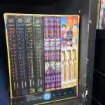 A box set of Batman, Joker, and Superman manga on a black shelf.