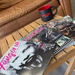 A few issues of the horror magazine "Fangoria" lie on a wooden table, along with a black and red mug that reads "Fangoria, since 1979).