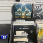 Vinyl record covers in a record flip bin. The visible records read "The Holy Bible Part 2" and "The Crystal Tears." There are dividers visible in the bins that read "805 Artists - LP's New," "Yay! Records," "Madlib & Related," "J Dilla & Related," and "BLU LP's."