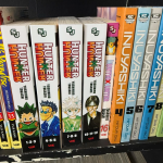 A collection of manga standing on its side on a shelf. The spines read "Hunter x Hunter" and "Inuyashiki."