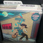 A vinyl record cover in a record flip bin by the artist Los Xiqueños. The record is priced at $17. There are two tab dividers visible in the bin that read "805 Artists - LP's New" and "Yay! Records."