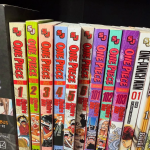 A collection of manga books on their sides on a shelf: One Piece and One-Punch Man