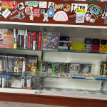 A wooden and glass display case containing a variety of handheld video game consoles and video game discs in their cases.