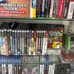 A glass display case containing Playstation 2 games (including The Simpsons Road Rage), Playstation 3 games, Playstation games, and Sega Genesis games.