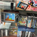 A glass display case holding Playstation 2 games, Playstation 3 games, a LEGO TV displaying Super Mario Bros, a LEGO NES console, and a box for Mario Kart Live Home Circuit.